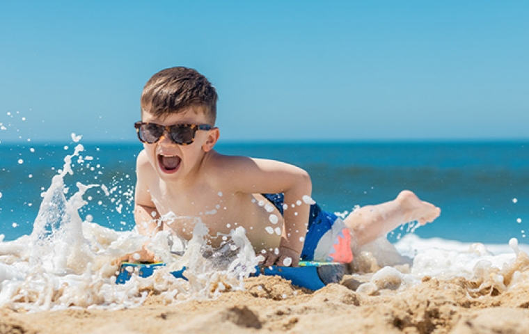 jongetje met zonnebril op speelt in het water op het strand